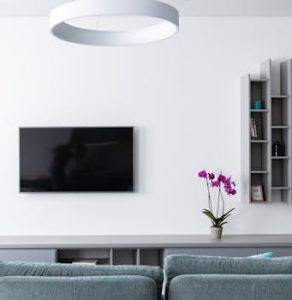 Comfortable modern living room with gray sofa and TV with shelves hanging on wall